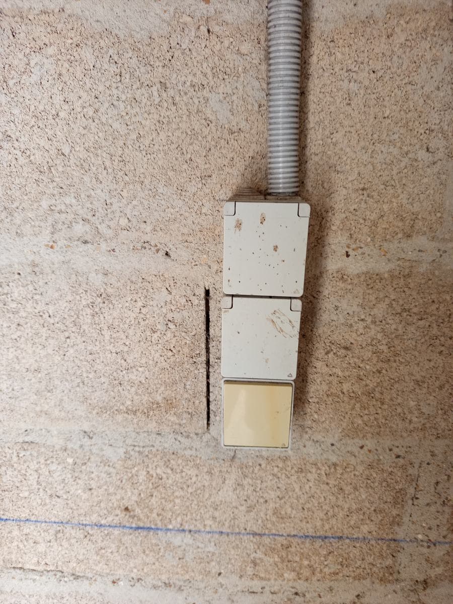 Anciens boîtiers électriques en saillie jaunis sur le mur en parpaing d'un garage, avant remplacement à Thoiry, Yvelines